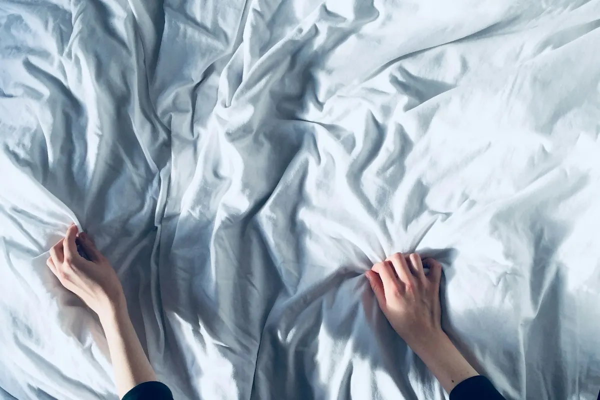 Manos estirando y alisando una sábana blanca arrugada sobre una cama