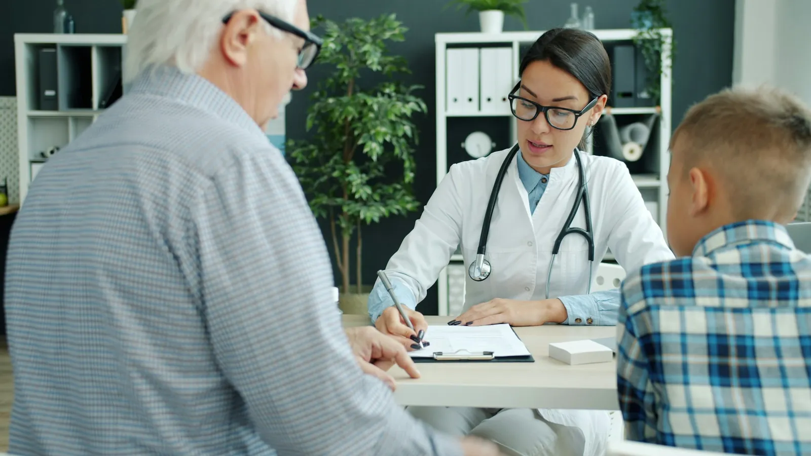 Médica atendiendo una consulta familiar con un adulto mayor y un niño