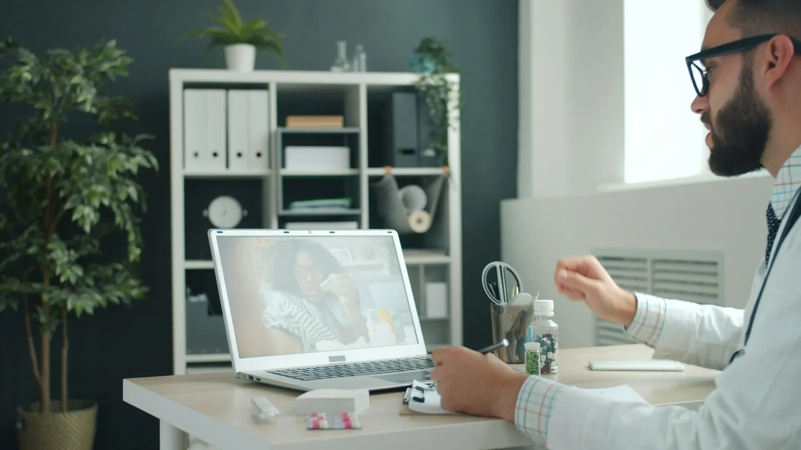 Médico atendiendo una videoconsulta desde su escritorio con un computador portátil