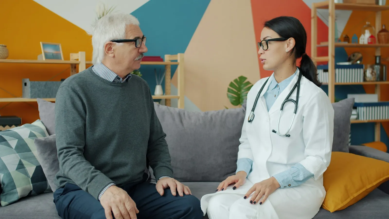 Médica conversando con un paciente mayor en el sofá de su casa durante una consulta a domicilio