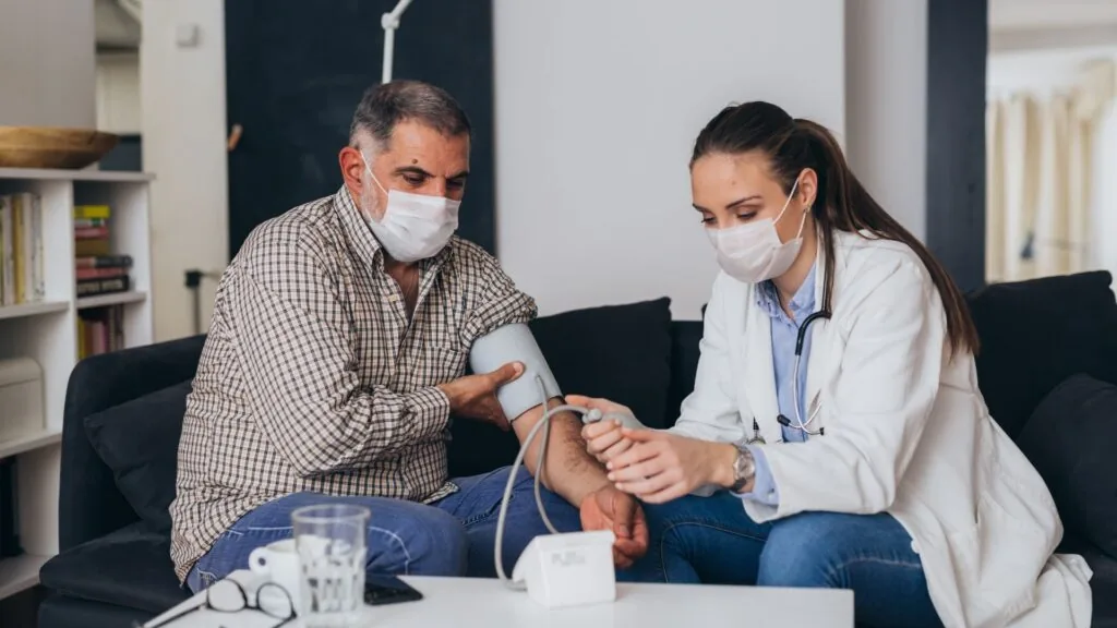 Médica controlando la presión arterial de un paciente en su hogar