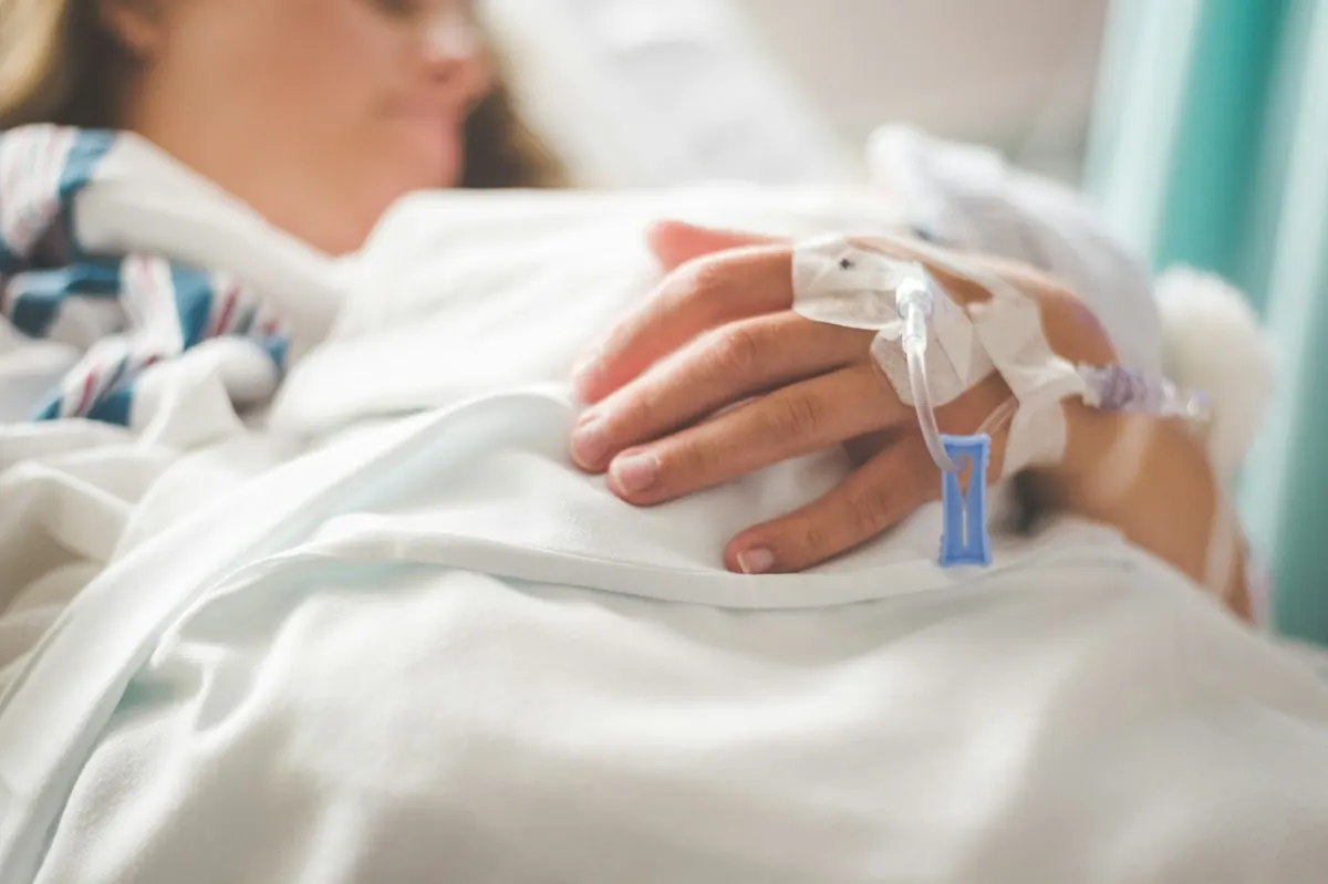 Mano de un paciente con una vía de suero puesta, apoyada sobre la sábana