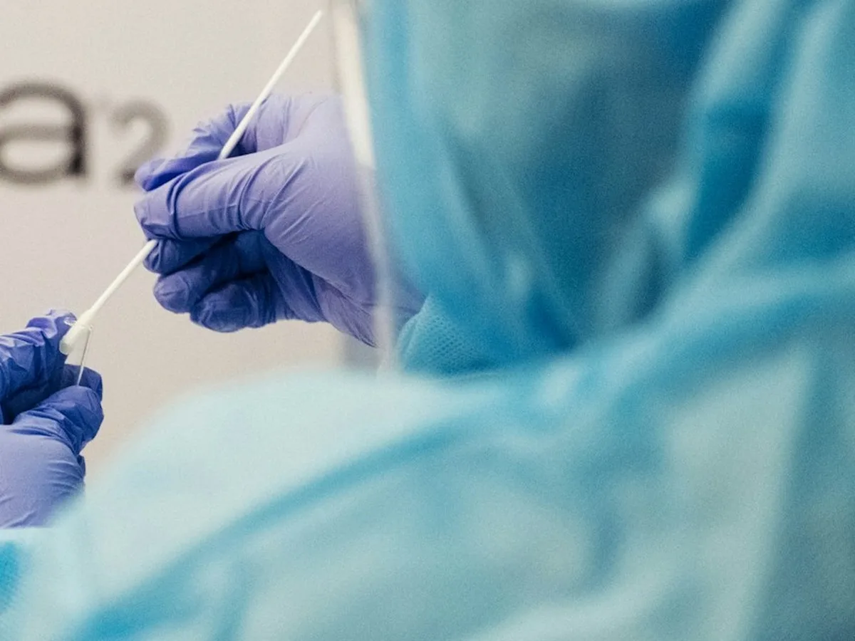 Profesional de la salud con traje y guantes de protección sosteniendo un hisopo para una prueba de COVID-19